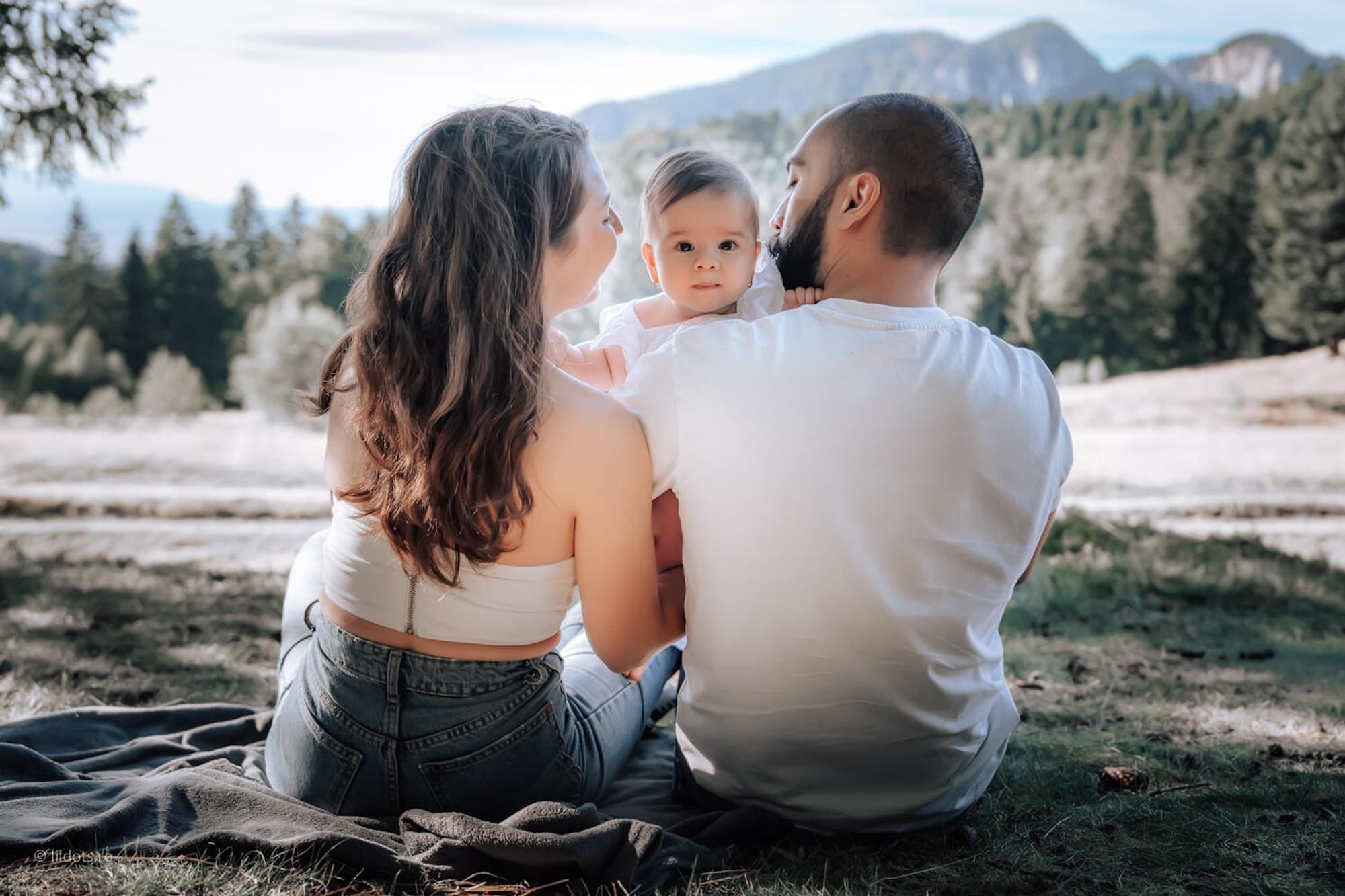 Familie văzută din spate, așezată pe o pătură, privind munții