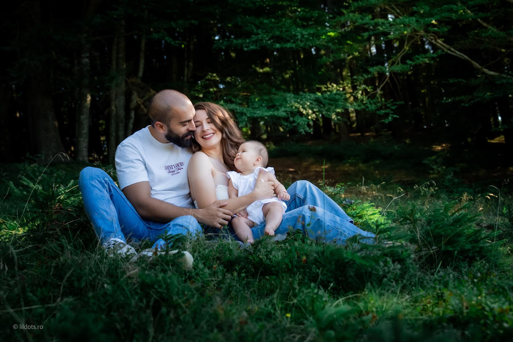 Familie așezată în iarba înaltă, într-⁠o rază de lumină din pădure